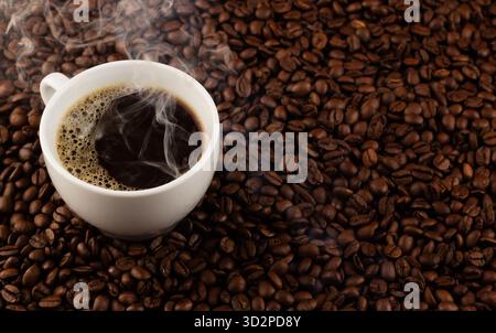 Heiße Tasse schwarzen Kaffee umgeben von gerösteten Kaffeebohnen auf einem Tisch Stockfoto