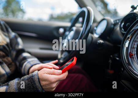 Autofahrerin, die online über das Smartphone in sozialen Medien scrollt, Nachrichten beantwortet, Nachrichten auf dem Telefon liest. Stockfoto