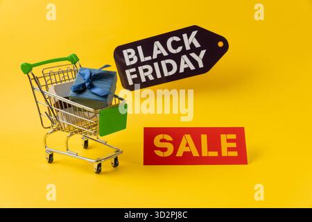 Miniatur-Einkaufswagen mit Geschenkbox für schwarzen freitag-Shopping auf gelbem Hintergrund Stockfoto