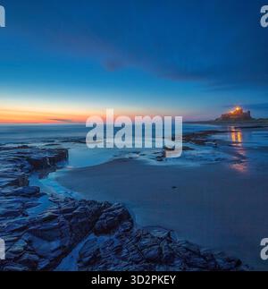 Ein Blick im Sommer bei Sonnenaufgang auf Bamburgh Castle mit Blick über den Strand bei Ebbe in Northumberland mit einem schönen Sonnenaufgang Stockfoto