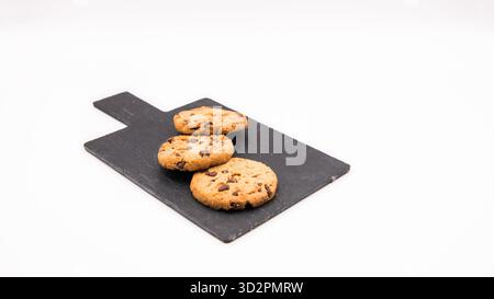 Frisch gebackene Schokoladen-Chips-Kekse auf einer kleinen Schieferplatte. Stilvolle, moderne Präsentation zum Fotografieren von Desserts oder Snacks. Stockfoto