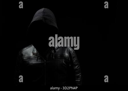 Nahaufnahme eines gesichtslosen Hacker-Mannes mit Kapuze im Schatten links auf dem Bildschirm und einem schwarzen Hintergrund Stockfoto