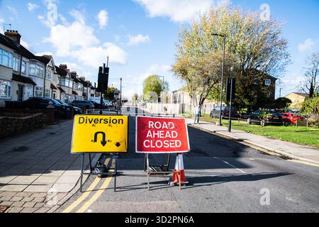 Rotes Schild „Road Ahead Closed“ neben einem gelben Umleitungsschild am Straßenrand, das die Fahrer vor einer Straßensperrung und einer alternativen Route im Vereinigten Königreich warnt. Stockfoto