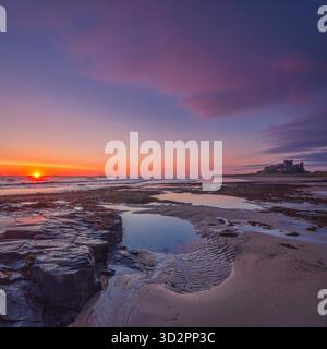 Ein Blick im Sommer bei Sonnenaufgang auf Bamburgh Castle mit Blick über den Strand bei Ebbe in Northumberland mit einem schönen Sonnenaufgang Stockfoto