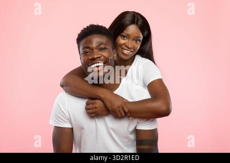 Das junge Paar teilt eine freudige Umarmung im Studio mit rosa Hintergrund Stockfoto