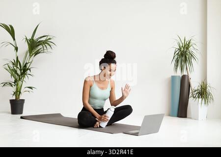 Junge sportliche Frau genießt Online-Yoga-Kurs zu Hause im Bright Studio mit Laptop Stockfoto