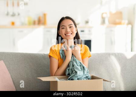 Überglückte Frau, die nach der Lieferung auf ihrem Sofa Online-Bestellung auspackt und die Kamera anlächelt Stockfoto