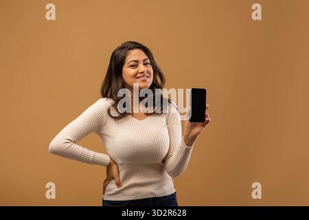 Glückliche junge arabische Frau zeigt modernes Smartphone mit leerem Bildschirm, empfiehlt mobile App oder Angebot, Mockup Stockfoto