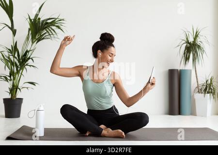 Fröhliche junge Frau genießt Musik, während sie während des Workouts auf der Yogamatte sitzt Stockfoto