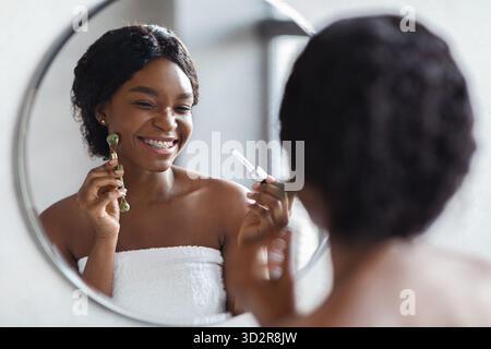 In einem hellen Badezimmer steht eine junge afroamerikanische Frau vor einem Spiegel Stockfoto