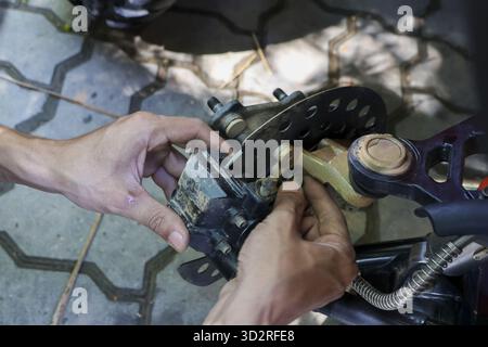 Nahaufnahme der fokussierten Mannhände, die den Bremssattel des Motorrads reparieren. Ein erfahrener Mechaniker führt detaillierte Wartungsarbeiten am Fahrzeug professionell durch Stockfoto