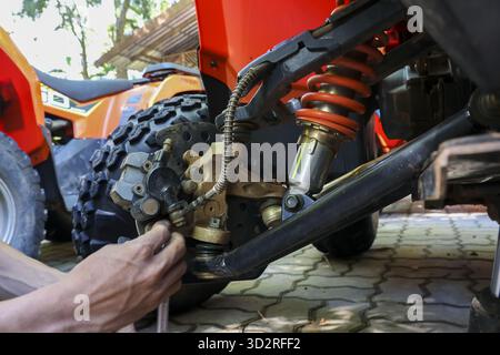 Fokussierte Mechaniker, die Fahrzeugreparaturen auf dem roten Quad durchführen. Man fixiert Federung und Stoßdämpfer mit Werkzeug, konzentriert auf Wartungsservice o Stockfoto