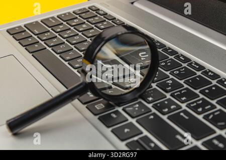 Eine Lupe befindet sich auf einer Laptop-Tastatur. Die Szene zeigt helle Farben und konzentriert sich auf die Details der Tasten, wodurch der Arbeitsbereich bei verbessert wird Stockfoto