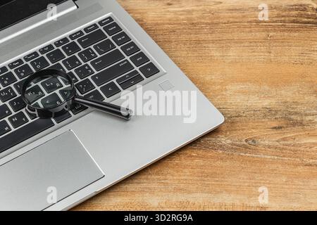 Eine Laptop-Tastatur ist mit einer Lupe auf den Tasten abgebildet, die den Fokus auf Details und Technologie unterstreicht. Die Einrichtung hat einen Holztisch Stockfoto