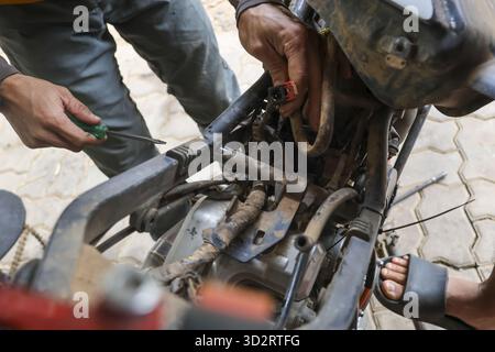 Hände eines Mechanikers, der mit Werkzeugen am Motorradmotor arbeitet, sich auf komplizierte Details konzentriert und sich für Reparaturen engagiert Stockfoto