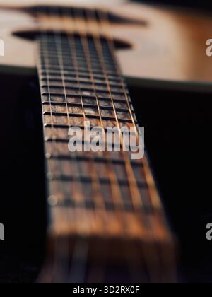 Warme Gitarrenaufnahme mit sanftem Sonnenlicht, Fokus auf den Hals im Vordergrund, verschwommener Körper im Hintergrund, subtile Schatten am Hals, gemütlich und mi Stockfoto