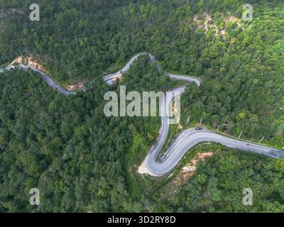 Die faszinierende Aussicht aus der Vogelperspektive zeigt die gewundene Straße, die sich durch dichte grüne Waldlandschaft schlängelt. Berggelände bietet atemberaubende Naturreisen, Einladungen Stockfoto