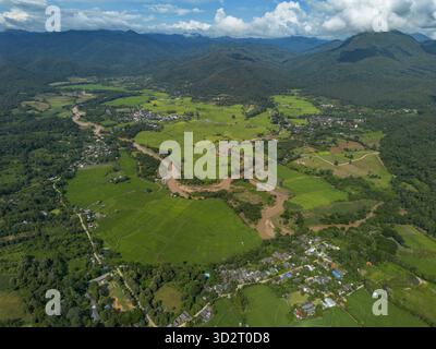 Panoramablick aus der Luft, üppige grüne Landschaft. Der sich windende braune Fluss fließt durch ein riesiges fruchtbares Tal. Abgelegenes Dorf eingebettet in grüne Natur. Outdo Stockfoto