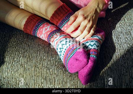 Frau massiert die Wadenmuskulatur durch bunte Stricksocken mit geometrischem Norwegermuster. Steht für Selbstmassage, Fußgesundheit und Wellness zu Hause. Stockfoto