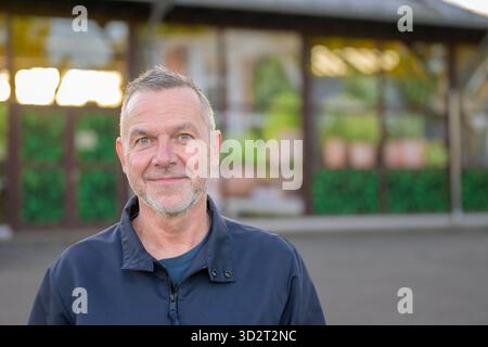 Porträt eines selbstbewussten, Reifen Mannes, der draußen bei weichem Tageslicht steht und ruhig in die Kamera lächelt. Stockfoto