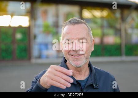 Fröhlicher reifer Mann mit geschlossenen Augen, der tagsüber natürlich in einer urbanen Umgebung lächelt. Stockfoto