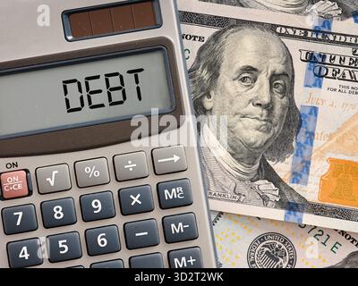 Der Rechner zeigt Schulden auf dem Bildschirm mit hundert Dollar-Scheinen darunter an und veranschaulicht die Finanzkrise und die wirtschaftlichen Probleme Stockfoto