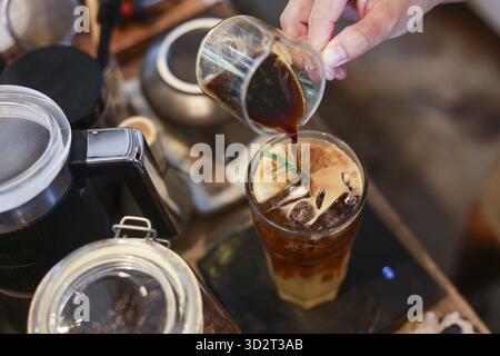 Ein fokussierter Barista bereitet erfrischende Getränke zu und gießt schwarzen Kaffee in ein Glas für die kalte Zubereitung. Dieser Prozess der Herstellung eines belebenden Eiskaffee-Getränks Stockfoto
