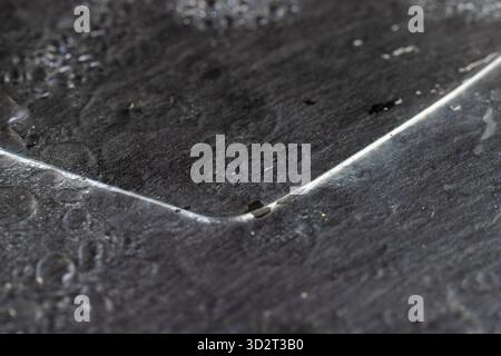 Zerbrochenes, nasses altes Glas liegt auf einem schwarzen Schieferbrett mit einer ungleichmäßigen Textur, Stücke von gebrochenem transparentem Glas, das in der Konstruktion verwendet wird, mit Wasser-dr bedeckt Stockfoto