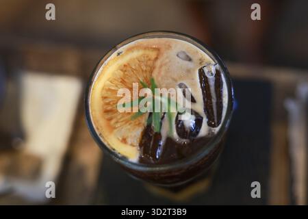 Erfrischendes Glas Eiskaffee mit Orangen- und Kräutergarnitur. Dieses köstliche Getränk im Café, das perfekte kühle Getränk für einen warmen Sommertag, Top VI Stockfoto
