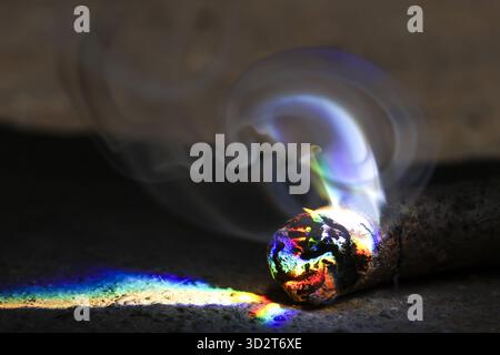 Geheimnisvoller Abstract des schwelenden Glimmers, der Rauch und ein wunderschönes Regenbogenlichtspektrum erzeugt. Feuer erzeugt in dieser magischen Magie einen Prismeneffekt auf dunkler Oberfläche Stockfoto