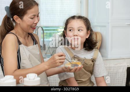 Gemeinsame Aktivitäten während der Feiertage. Eltern und Kinder essen zusammen, Mutter bereitet das Frühstück für die Tochter am Morgen vor, genießen Sie, kleine Stockfoto
