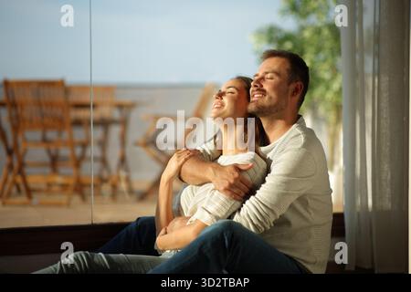 Glückliches verliebtes Paar genießt gemeinsam am Fenster zu Hause einen sonnigen Tag Stockfoto