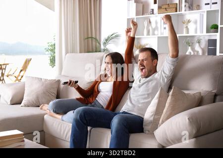 Ein aufgeregtes Paar sieht fern und feiert auf einer Couch zu Hause Stockfoto