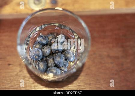 Frische Schüssel mit Heidelbeerfrüchten in klarem Glas auf braunem Holztisch. Diese Nahaufnahme aus einem hohen Winkel erzeugt ein einfaches, gesundes und gesundes Gefühl für nat Stockfoto