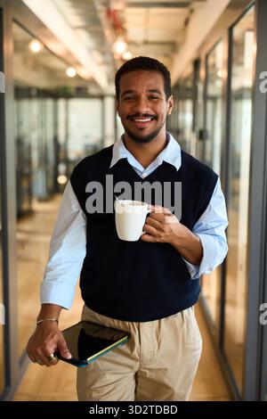 Lächelnder lateinamerikanischer Geschäftsmann bei Kaffeepause im modernen Büroflur Stockfoto