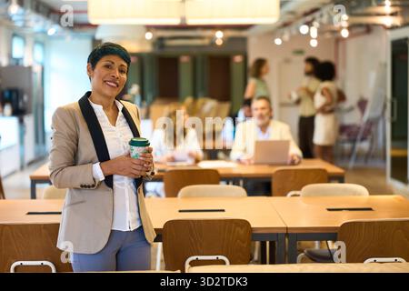 Lateinische Geschäftsfrau lächelt mit Kaffeetasse in einem modernen Coworking Office Stockfoto
