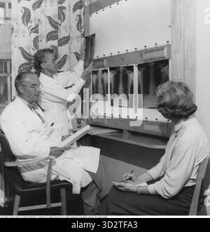 Im Krankenhaus 1956. Ein männlicher und weiblicher Arzt, der Röntgenbilder der Brust der Menschen untersucht, die Brustkorb und Lunge zeigen. Conard Ref. 3051 Stockfoto