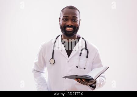 Afroamerikaner Arzt lächelt selbstbewusst, während er ein Notizblock hält, Studioporträt mit Kopierraum. Stockfoto