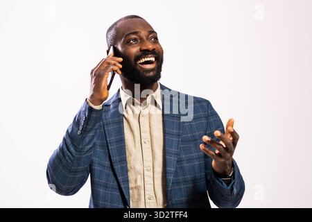 Selbstbewusster afroamerikanischer Geschäftsmann lacht, während er in einem Studio mit seinem Smartphone spricht, einen Anzug trägt und Glück ausstrahlt. Stockfoto
