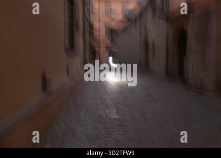 Ein abstrakter, bewegungsunscharfer Blick auf eine enge kopfsteingepflasterte Gasse, gesäumt von historischen Gebäuden in warmen Pfirsichfarben und Beigetönen. Weiches Dämmerungslicht und ein Bogen Stockfoto