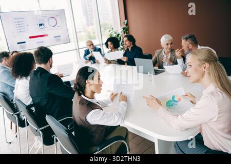 Verschiedene Teams arbeiten im Büro zusammen, diskutieren Ideen und tauschen Erkenntnisse in einer Gruppenbesprechung aus, die Berichte und Präsentationen umfasst Stockfoto
