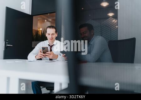 Zwei multikulturelle Geschäftsleute an einem Konferenztisch mit Smartphones in einem modernen Büro Stockfoto