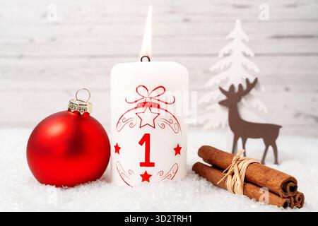 Bayern, Deutschland - 29. Oktober 2025: Die erste Adventskerze brennt zum ersten Adventstag. Eine weiße Kerze mit rotem Schriftzug und der Nummer 1 vor Weihnachtsdekoration *** erste Adventskerze zum ersten Adventsbrand. Eine weiße Kerze mit roter Schrift und mit der Zahl 1 vor weihnachtlicher Dekoration Stockfoto