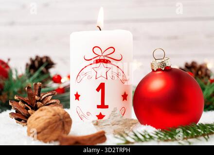 Bayern, Deutschland - 29. Oktober 2025: Die erste Adventskerze brennt zum ersten Adventstag. Eine weiße Kerze mit rotem Schriftzug und der Nummer 1 vor Weihnachtsdekoration *** erste Adventskerze zum ersten Adventsbrand. Eine weiße Kerze mit roter Schrift und mit der Zahl 1 vor weihnachtlicher Dekoration Stockfoto