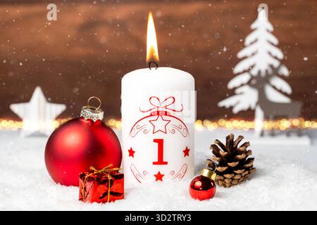 Bayern, Deutschland - 29. Oktober 2025: Die erste Adventskerze brennt zum ersten Adventstag. Eine weiße Kerze mit rotem Schriftzug und der Nummer 1 vor Weihnachtsdekoration *** erste Adventskerze zum ersten Adventsbrand. Eine weiße Kerze mit roter Schrift und mit der Zahl 1 vor weihnachtlicher Dekoration Stockfoto