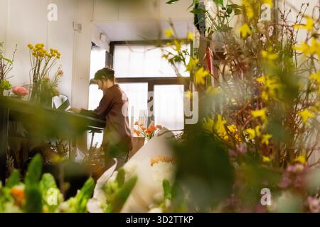 Die Floristin arbeitet mit einem Laptop und nimmt Bestellungen online im Blumenladen an Stockfoto