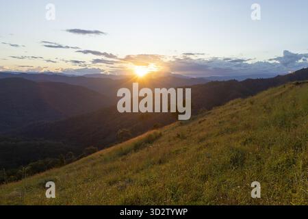 Wunderschöner, ruhiger Sonnenuntergang über dem grasbewachsenen Berg. Goldenes Licht der Sonne, das über friedliche Landschaft strahlt, schafft ein ruhiges und warmes Gefühl von Hoffnung A Stockfoto