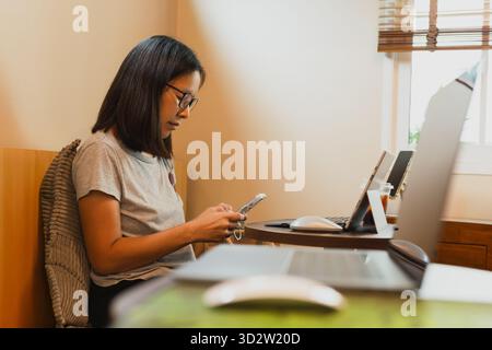 Die Frau benutzt das Handy, während sie im Café mit dem Laptop arbeitet. Stockfoto