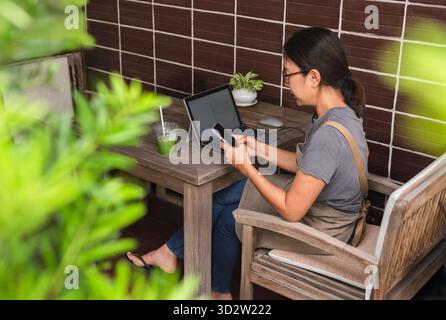 Frau Hand mit Mobiltelefon, während sie im Freien mit einem Laptop arbeitet. Stockfoto