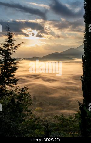 Ein Bergtal am Morgen, wo die Herbstsonne durch die Wolken bricht, um ihr Licht zu werfen, und den Talnebel in Goldfarbe taucht. Stockfoto